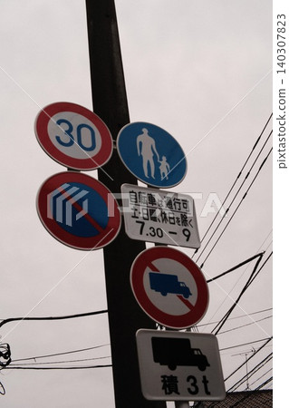 Multiple road signs, including speed limit signs, are posted on a utility pole under a cloudy sky. Multiple road signs, including speed limit signs, are posted on a utility pole under a cloudy sky. 140307823