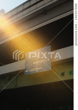A blue road sign installed under an elevated structure where bright sunlight streams in. A blue road sign installed under an elevated structure where bright sunlight streams in. 140307899