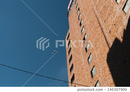 Airplanes flying in a cloudless blue sky and tall brick buildings Airplanes flying in a cloudless blue sky and tall brick buildings 140307900
