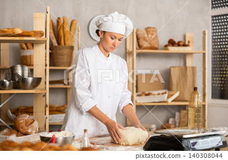 Woman works in bakery as baker, kneads dough, works with flour. Woman works in bakery as baker, kneads dough, works with flour. 140308044