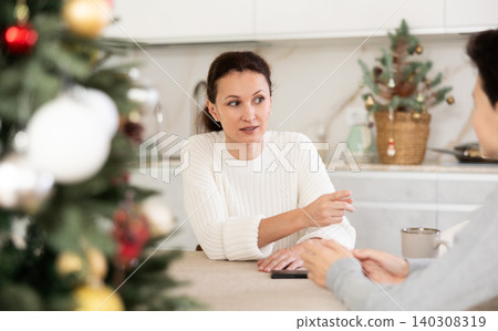 Mother and teenage son drinking tea in kitchen and chatting while celebrating Christmas Mother and teenage son drinking tea in kitchen and chatting while celebrating Christmas 140308319