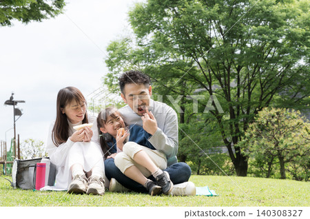 一家人其樂融融地在草地上享受假期，臉上洋溢著笑容；一位愛玩的爸爸在野餐時吃著三明治午餐；全身照。 140308327