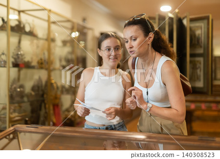 Young woman with teen daughter visitors stands near horizontal glass display case Young woman with teen daughter visitors stands near horizontal glass display case 140308523