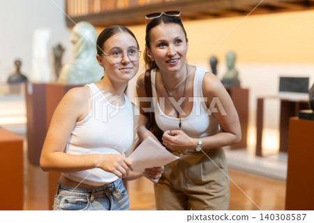 Young woman with teen daughter walk around museum, view sculpture in museum hall 140308587