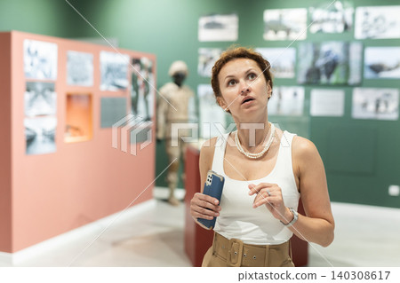 Interested woman observing exhibit of military outfit in museum 140308617
