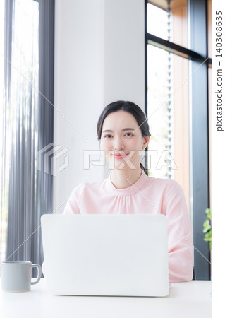 一位身穿粉紅色洋裝的美麗女子坐在辦公室的桌子前,正在使用電腦,並直視鏡頭。 一位身穿粉紅色洋裝的美麗女子坐在辦公室的桌子前,正在使用電腦,並直視鏡頭。 140308635