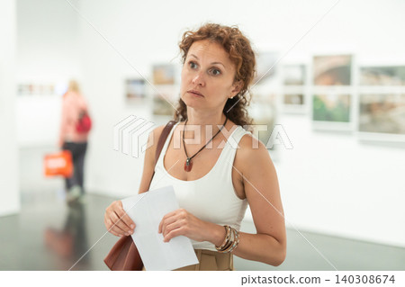Thoughtful woman examining photographs on walls in art gallery Thoughtful woman examining photographs on walls in art gallery 140308674