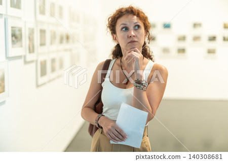 Woman observing photographs on display in photo gallery Woman observing photographs on display in photo gallery 140308681