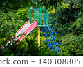 A colorful park slide surrounded by green trees 140308805
