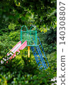 A colorful park slide surrounded by green trees 140308807