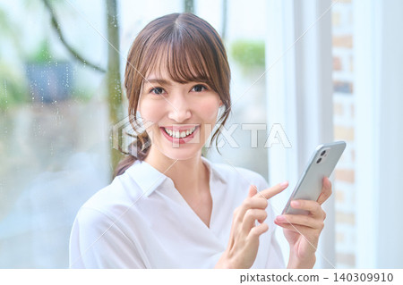 A woman smiles while operating her smartphone. A woman smiles while operating her smartphone. 140309910