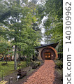 A modern building nestled in a lush green forest, with a wood chip approach. 140309962