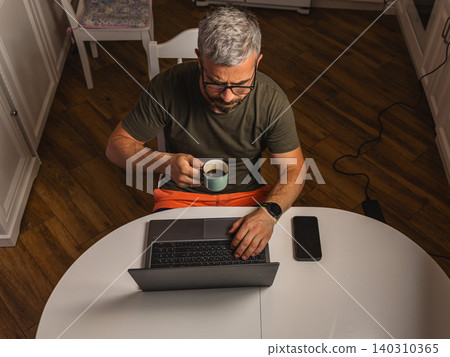 Man enjoying coffee while working from home at a kitchen table 140310365