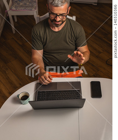 Man enjoys coffee while working on laptop at home in the morning 140310366