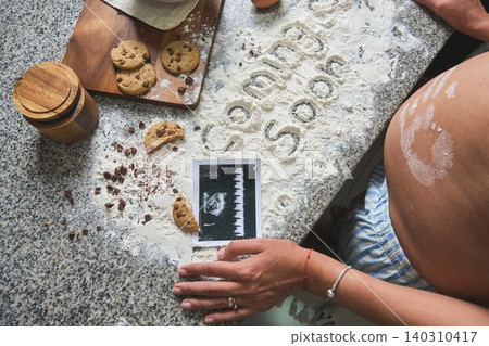 Pregnant woman making baby announcement with flour and cookies Pregnant woman making baby announcement with flour and cookies 140310417