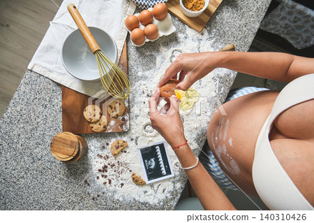 Pregnant woman baking cookies showing baby ultrasound scan Pregnant woman baking cookies showing baby ultrasound scan 140310426