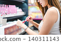 Gen z woman shopping for cosmetics in a modern beauty store choosing makeup trend products on shelf 140311143