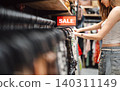 Young adult woman gen Z shopping choosing used clothing second hand shop fast fashion lifestyles 140311149