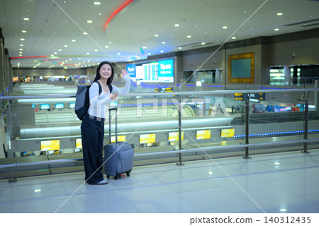 Young woman traveler smiling using smartphone with luggage in airport terminal Young woman traveler smiling using smartphone with luggage in airport terminal 140312435