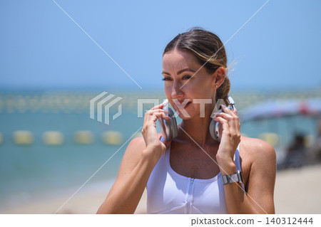 Young sporty woman with headphones getting ready for exercise by the sea. Young sporty woman with headphones getting ready for exercise by the sea. 140312444