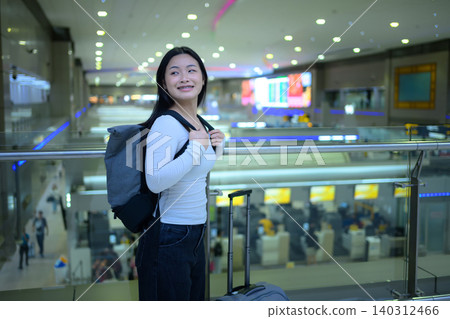 Gen Z traveler smiling with backpack and suitcase at airport terminal 140312466