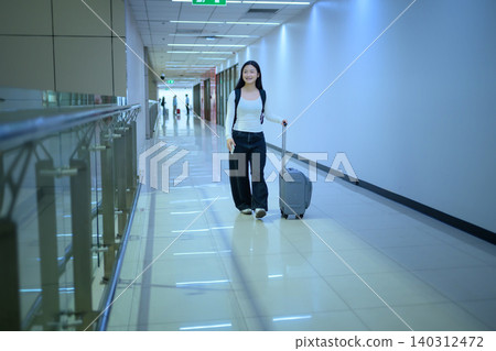 Gen Z traveler walking with suitcase smiling in airport corridor 140312472