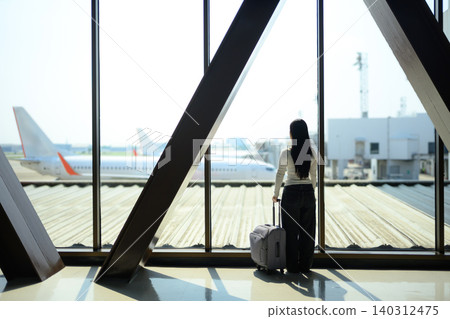 Gen Z young woman traveler waiting with suitcase watching airplane at airport window Gen Z young woman traveler waiting with suitcase watching airplane at airport window 140312475