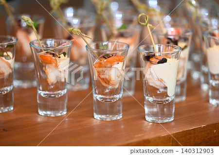 Shrimp cocktail appetizers served in small shot glasses with white sauce and microgreens on wooden table close up view Shrimp cocktail appetizers served in small shot glasses with white sauce and microgreens on wooden table close up view 140312903