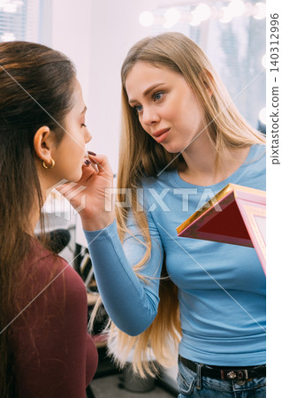 Beauty treatment. Cosmetic service. Makeup professional applying care product for woman facial rejuvenation in studio indoor. Beauty treatment. Cosmetic service. Makeup professional applying care product for woman facial rejuvenation in studio indoor. 140312996