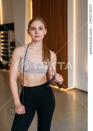 Athletic girl posing. Healthy lifestyle. Young female in modern sportswear holding jumping rope in studio. Body physical training indoors. Athletic girl posing. Healthy lifestyle. Young female in modern sportswear holding jumping rope in studio. Body physical training indoors. 140313025