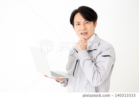 一位身穿灰色工作服的中年商人，在白色背景前，正看著他的筆記型電腦，若有所思。 140313333