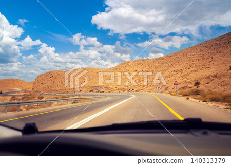 Driving a car on the mountain road in the desert. View of sandstone mountains through the windscreen. The road from Arad to the Dead Sea. Israel Driving a car on the mountain road in the desert. View of sandstone mountains through the windscreen. The road from Arad to the Dead Sea. Israel 140313379