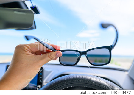 A hand holding sunglasses inside a car A hand holding sunglasses inside a car 140313477