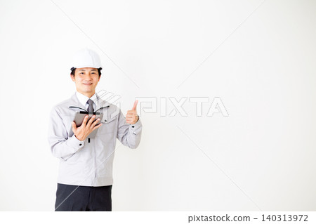 A middle-aged businessman in gray work clothes and a helmet, holding a tablet and making a triumphant gesture, against a white background. A middle-aged businessman in gray work clothes and a helmet, holding a tablet and making a triumphant gesture, against a white background. 140313972