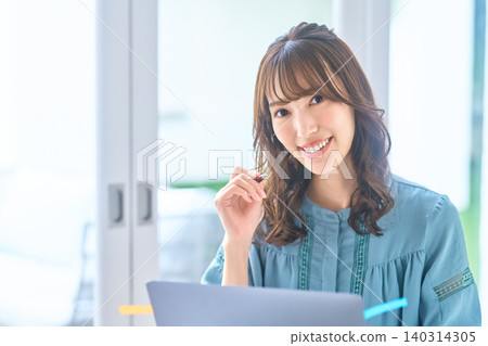 一位在家工作的女士面帶微笑,手裡拿著一支筆,直視著鏡頭。 一位在家工作的女士面帶微笑,手裡拿著一支筆,直視著鏡頭。 140314305