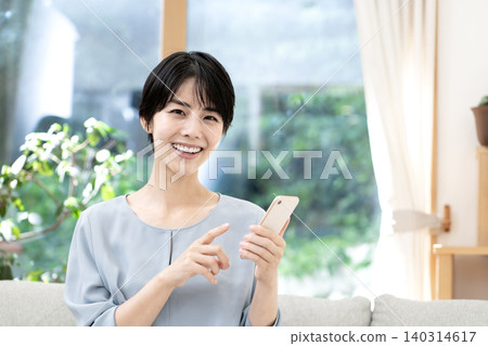 A young woman relaxing on her sofa at home and using her smartphone. A young woman relaxing on her sofa at home and using her smartphone. 140314617