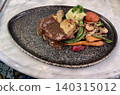 Close up of a dish of chicken steak with black pepper sauce and vegetables, served on an elegant stone black plate. 140315012