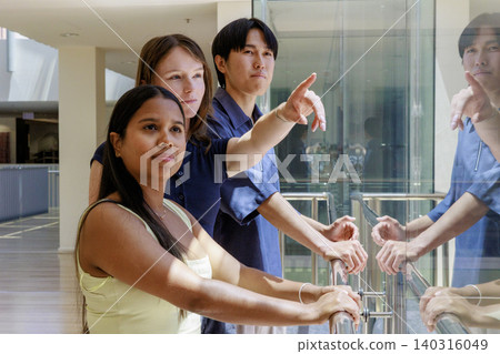 A group of students looking out the window at the sunny campus outside. A group of students looking out the window at the sunny campus outside. 140316049
