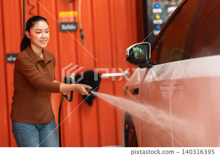 woman washing car with water hose in a self-service car wash station woman washing car with water hose in a self-service car wash station 140316395