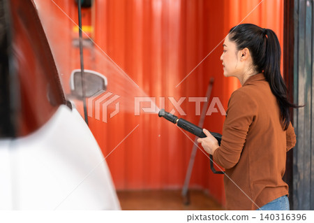 woman washing car with water hose in a self-service car wash station woman washing car with water hose in a self-service car wash station 140316396