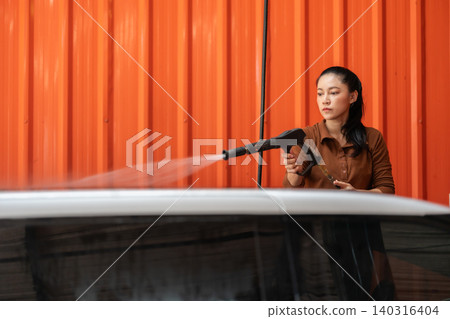 woman washing car with water hose in a self-service car wash station woman washing car with water hose in a self-service car wash station 140316404