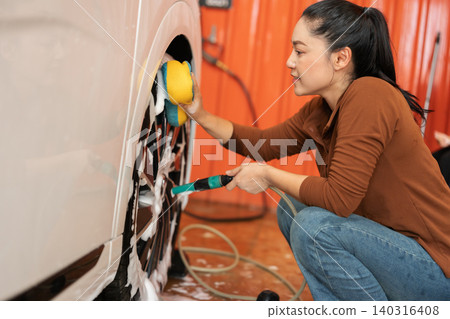 woman washing car wheel with sponge and foam in a self-service car wash station woman washing car wheel with sponge and foam in a self-service car wash station 140316408