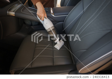 close up hand of woman using portable handheld vacuum cleaner to clean dust on leather car seat of electric car close up hand of woman using portable handheld vacuum cleaner to clean dust on leather car seat of electric car 140316413