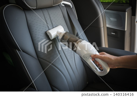 close up hand of woman using portable handheld vacuum cleaner to clean dust on leather car seat of electric car close up hand of woman using portable handheld vacuum cleaner to clean dust on leather car seat of electric car 140316416
