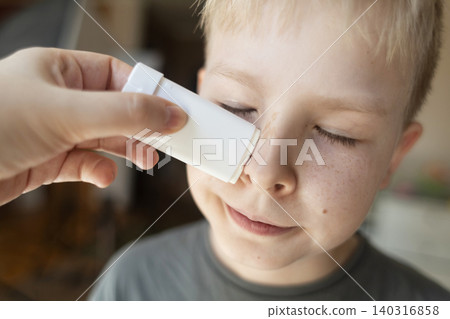 Mother applying sunscreen stick to her 10 year old son's face. Close up of boy closing eyes during mineral SPF protection application at home. Mother applying sunscreen stick to her 10 year old son's face. Close up of boy closing eyes during mineral SPF protection application at home. 140316858
