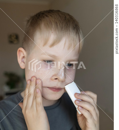 Cute 10 years old boy applying mineral sunscreen stick on his face. Caucasian child protecting freckled skin from sun damage with spf stick at home. 140316868