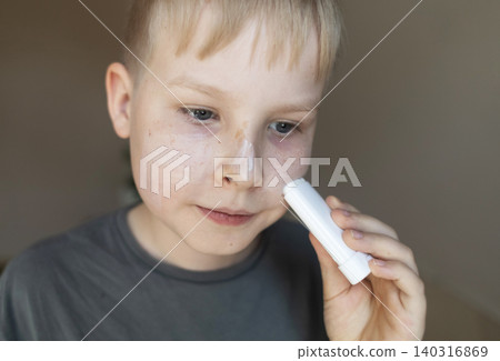 Cute 10 years old boy applying mineral sunscreen stick on his face. Caucasian child protecting freckled skin from sun damage with spf stick at home. 140316869