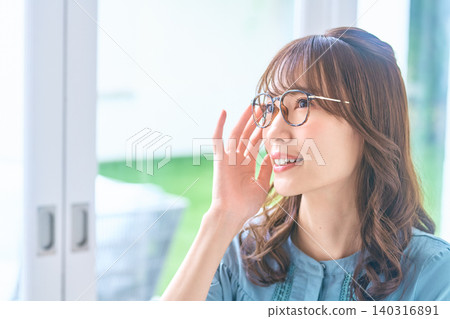 A young woman looks up from the window, her hand on her glasses. A young woman looks up from the window, her hand on her glasses. 140316891