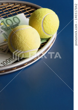 Two yellow tennis balls lie on a racket among one hundred euro and one hundred dollar bills Two yellow tennis balls lie on a racket among one hundred euro and one hundred dollar bills 140317842