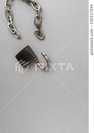 An open rusty padlock lying separated from a broken metal chain on a plain gray background. An open rusty padlock lying separated from a broken metal chain on a plain gray background. 140317844